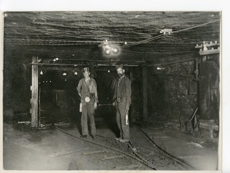 Two coal miners inside the mines standing on the tracks